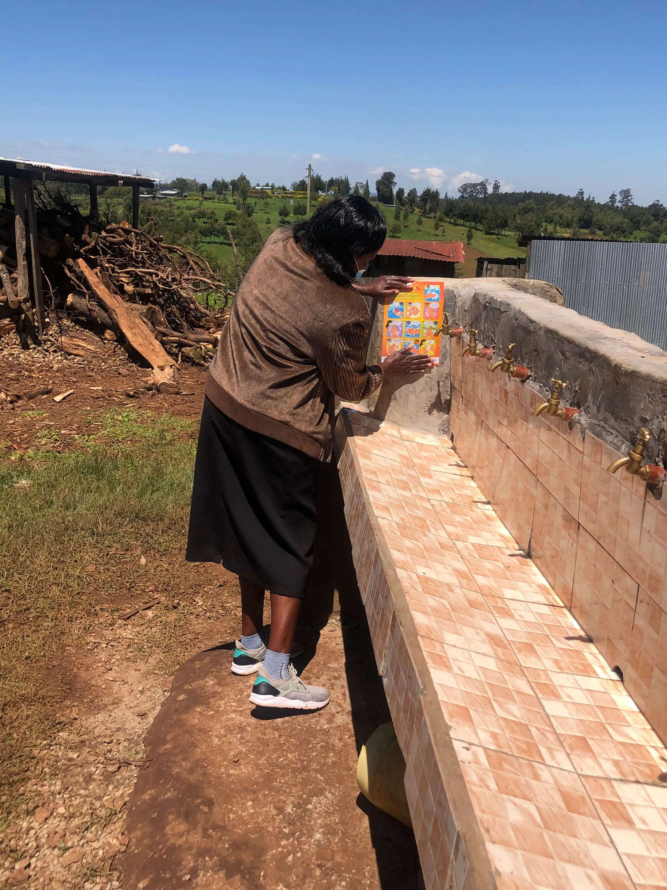 Head teacher at Chepketeret primary school stands next to the new handwashing station and shares documentation of the 10 steps for handwashing