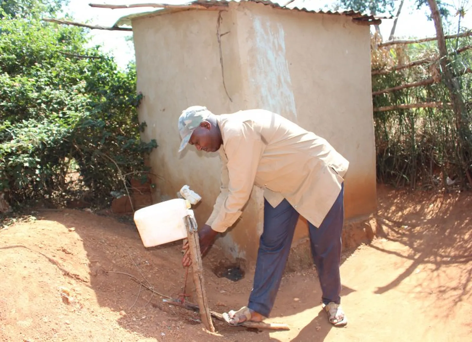 Twagilimana Frederic washing his hands after using the latrine (behind him).