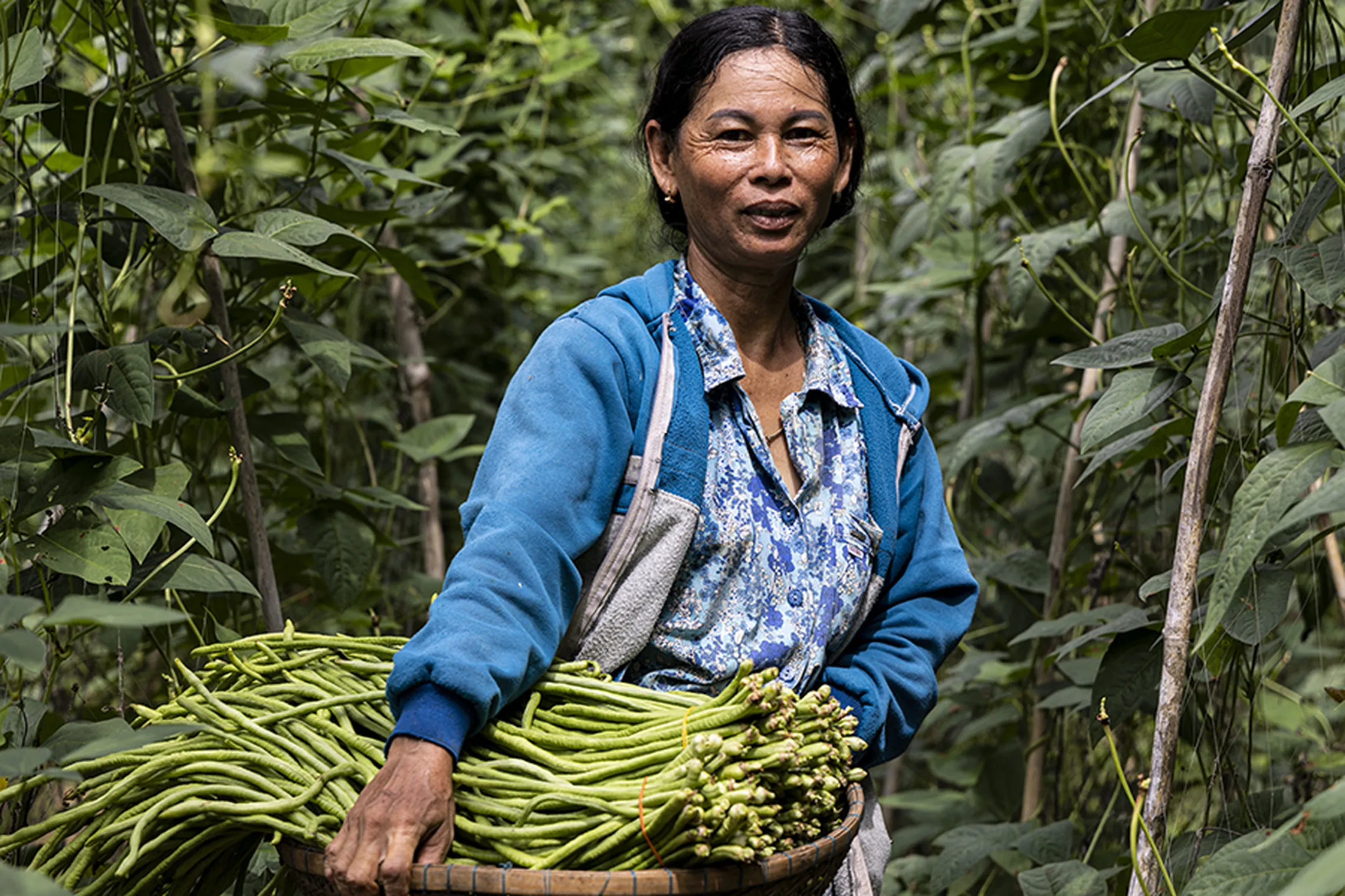 Srouy posing for a photo while holding a basket of beans