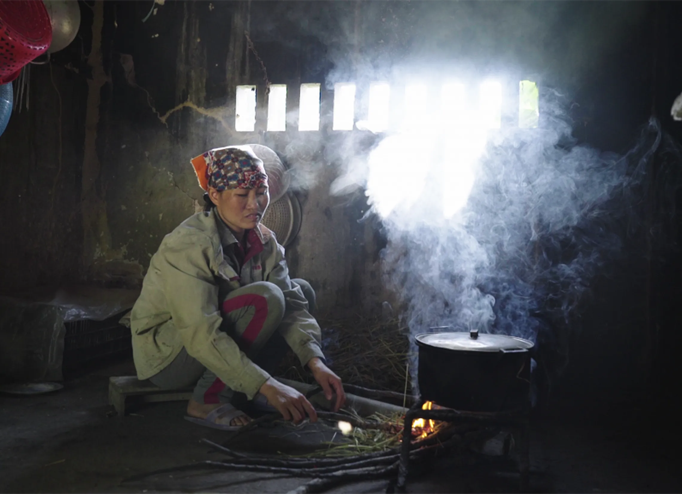 A traditional stove user tends the fire while exposed to harmful emissions